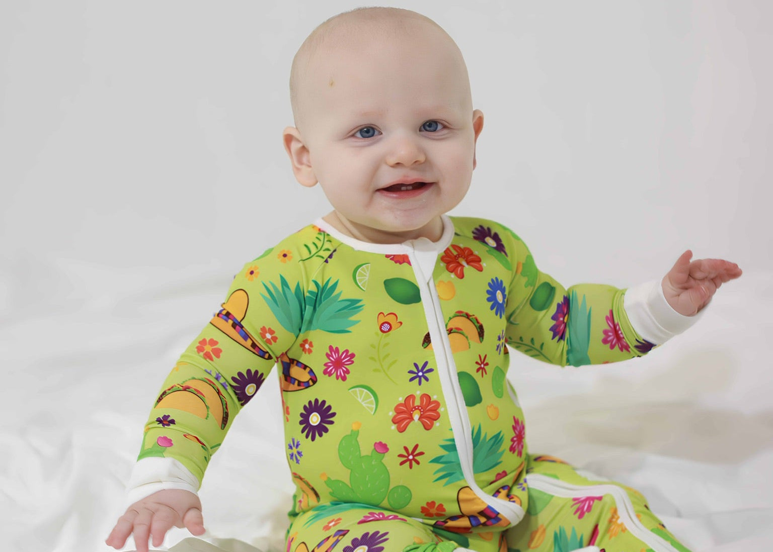 Baby wearing a colorful green onesie with taco pattern on a white background